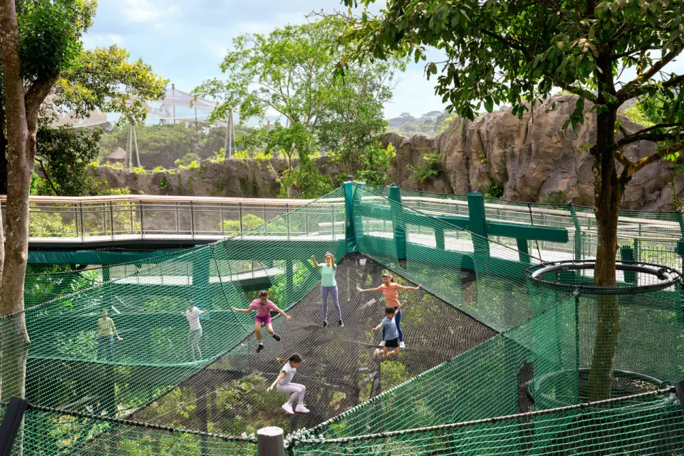 Children joyfully play and bounce on a large green rope net structure at "Curiosity Cove" in Asia Rainforest Adventure, enjoying an active outdoor exploration.
