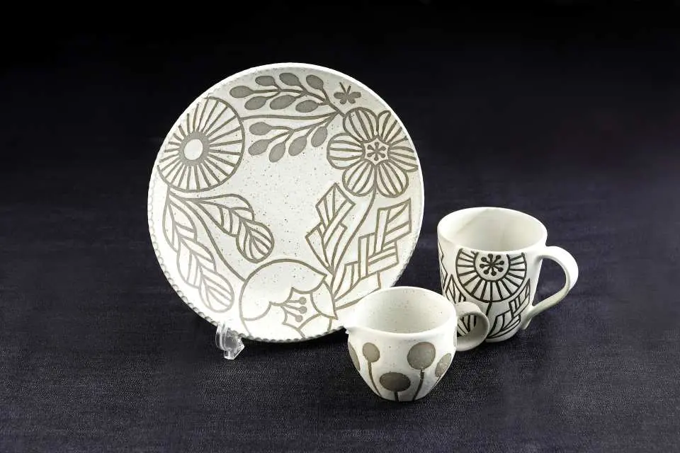 A unique handmade pottery dinnerware set from Sapporo Mono Village, including plates and cups adorned with elegant floral patterns, showcasing Hokkaido's craft aesthetics.