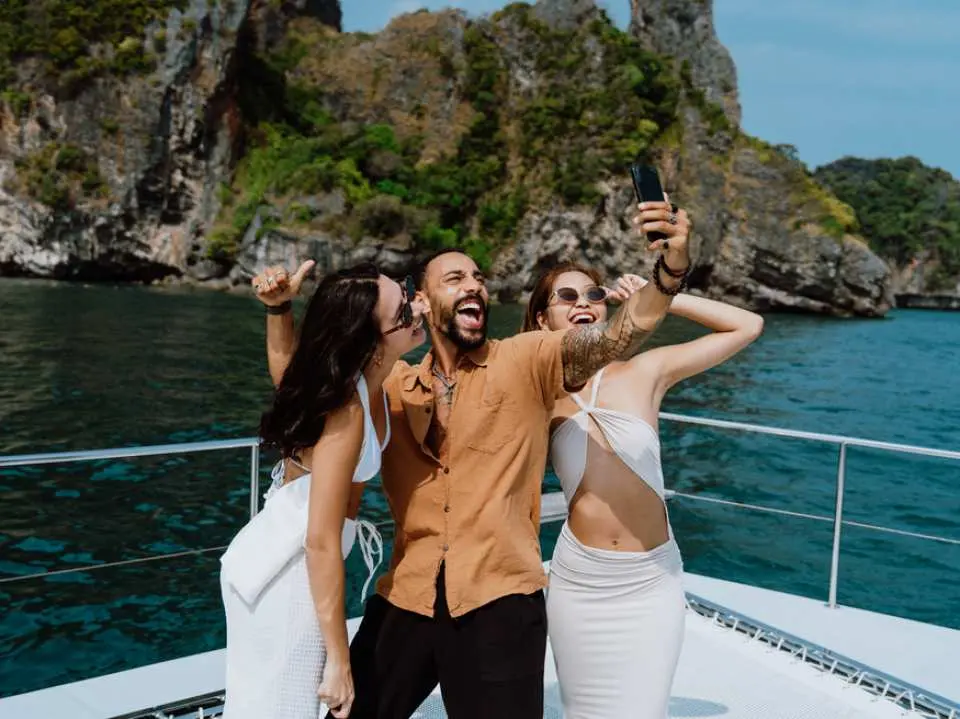 นักท่องเที่ยวมีความสุขบนดาดฟ้าเรือยอชต์สุดหรูในกระบี่ กำลังถ่ายเซลฟี่ เก็บภาพความทรงจำที่สนุกสนานกับเกาะหินปูนที่สวยงามและทะเลระหว่างการล่องเรือ 4 เกาะ.