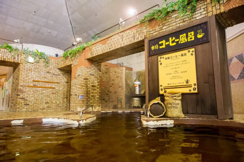 箱根小涌園ユネッサンのユニークなコーヒー風呂。茶色の湯気立つ湯面に、コーヒー豆袋と日本語の説明が添えられ、珍しい温泉体験を提供しています。