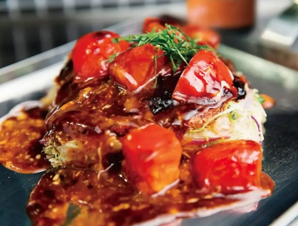Món okonomiyaki cà chua hảo hạng của chúng tôi được phục vụ kèm nước sốt làm từ Koshino Ruby của tỉnh Fukui. Món ăn này được làm từ bột bánh xèo mỏng theo công thức bí truyền kẹp cùng bắp cải thái sợi, tạo nên món ăn nhẹ và dễ ăn. Hương vị của Koshino Ruby và lá tía tô rất tinh tế, và khi bạn rưới nước sốt lên, chắc chắn nó sẽ trông rất tuyệt trên Instagram! ! Hãy thử một lần nhé! ! !
