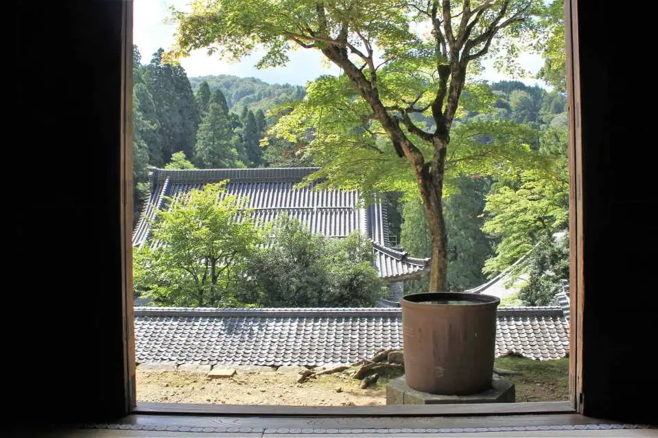 從日本福井永平寺窗框向外望去，可見傳統屋頂和茂密綠樹，營造出一種沉靜而充滿禪意的氛圍，讓人心靈放鬆。
