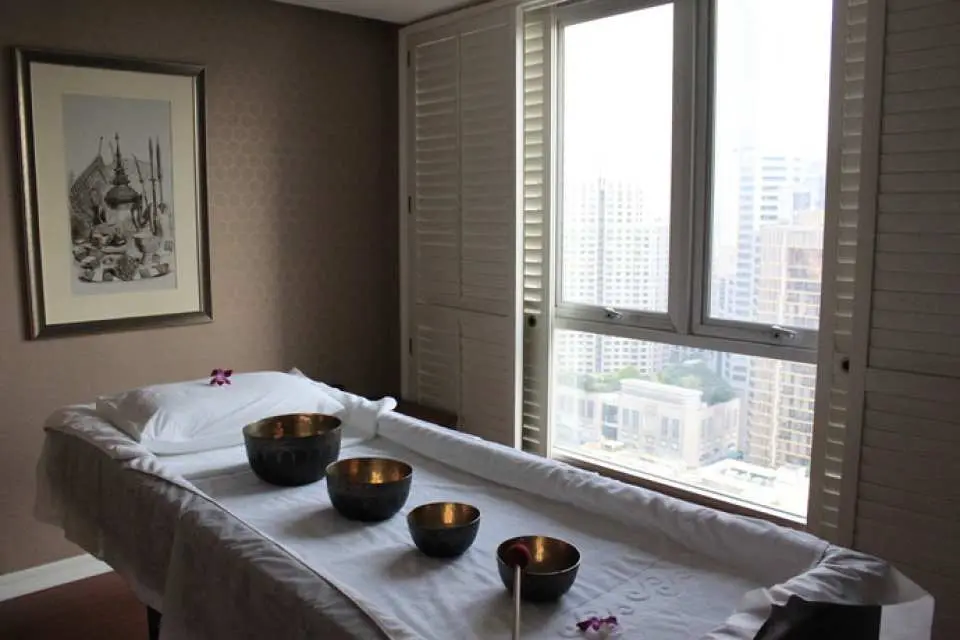 清迈 RarinJinda 健康水疗中心宁静的单人理疗室，按摩床上摆放着颂钵，窗外可见清迈市景，提供个人化的泰式按摩与身心疗愈。