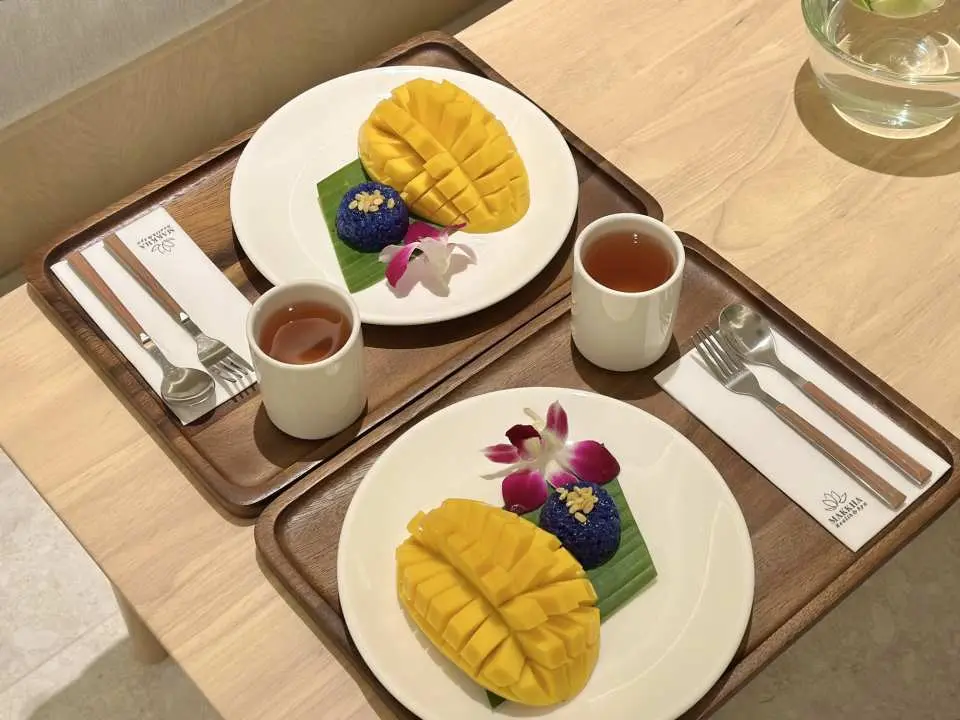 Makka Health & Spa独特餐点：两份精致摆盘的芒果糯米饭和热茶，让顾客在泰国水疗后品尝地道美味，享受悠闲时光。