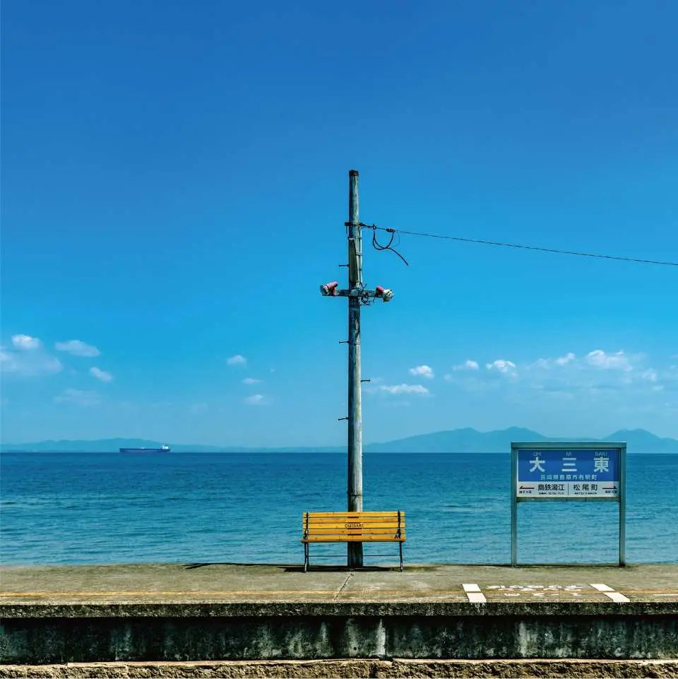 岛原“大三东车站”的黄色长椅，孤独地伫立在面海的月台上，背景是蔚蓝海水与晴朗天际。