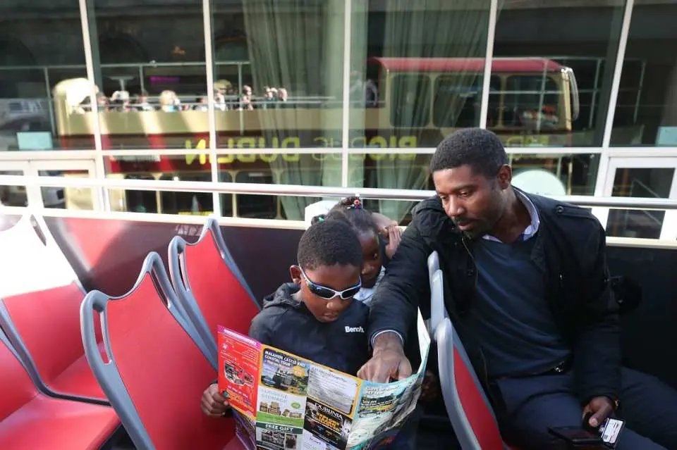 Du khách ngồi trên tầng trên của xe buýt du lịch hai tầng Big Bus Dublin mui trần, đọc bản đồ tuyến đường và tận hưởng chuyến đi thoải mái với hướng dẫn âm thanh đa ngôn ngữ và Wi-Fi miễn phí trên xe để chia sẻ.