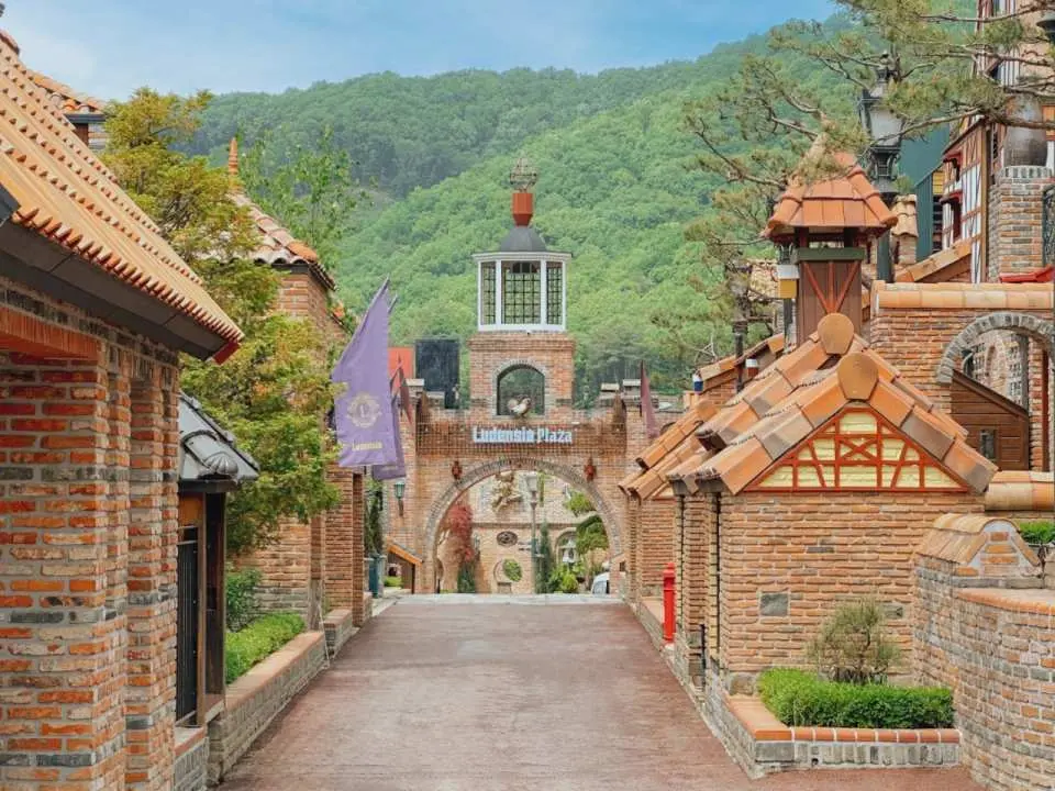 韓國驪州魯登西亞樂園的歐洲風格磚瓦小徑，兩旁是獨特的建築與拱門，遠處綠意盎然，是拍照打卡的理想地點。