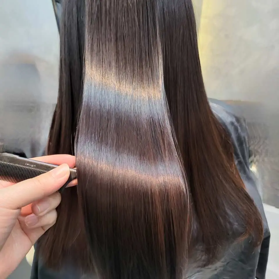 Close-up of professional hair care service at JUNG SAEM MOOL K-Beauty salon in Seoul, showing a stylist gently combing through long, shiny, healthy dark hair, highlighting the quality of the treatment.