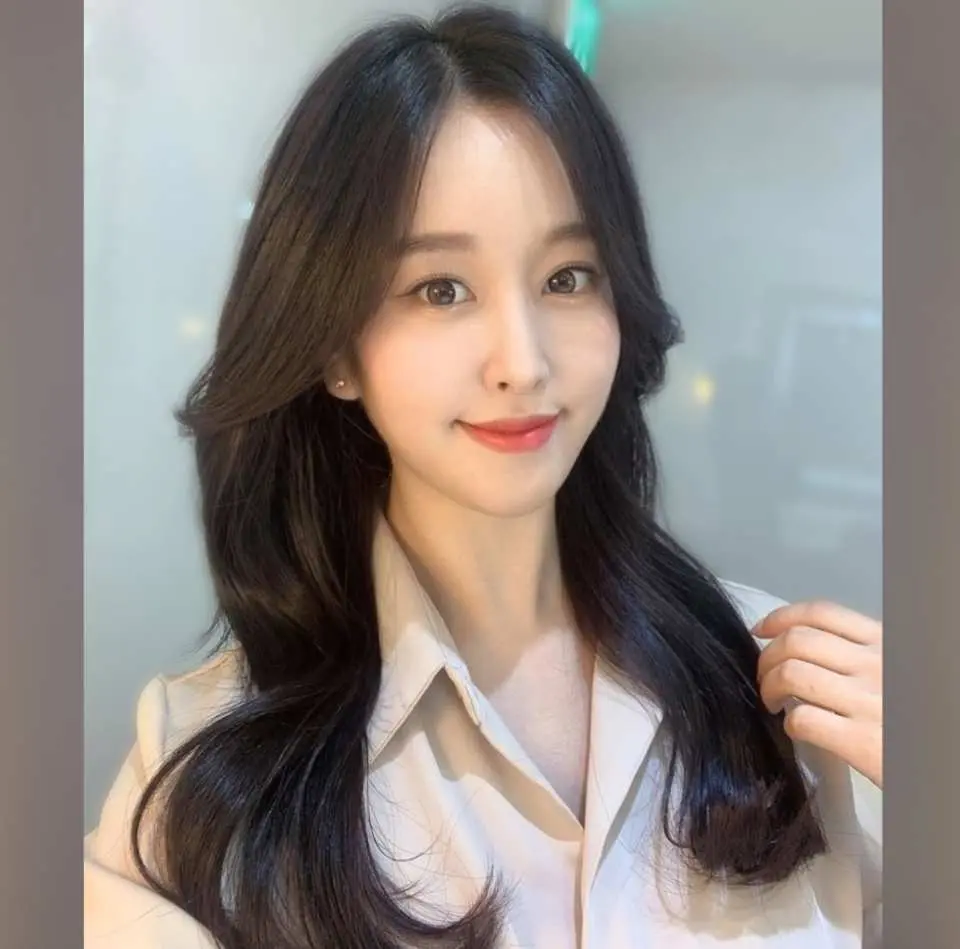 A woman with a bright, charming smile, natural makeup, and beautifully layered wavy black hair, showcasing a popular K-Beauty style from JUNG SAEM MOOL in Seoul, perfect for a personalized, radiant look.