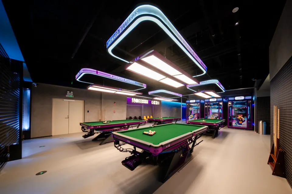 Modern billiard tables illuminated by stylish neon overhead lighting, alongside arcade machines, offering a trendy leisure zone at KP-FUN Shenzhen.