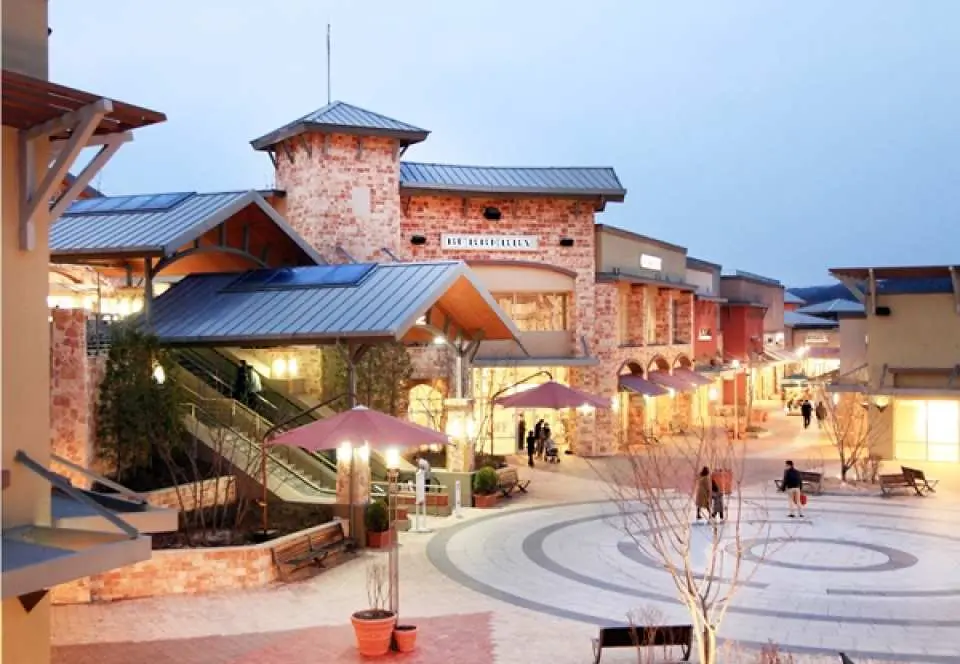 Gimpo Premium Outlets in Korea, with European-style architecture illuminated at dusk. Visitors enjoy fashion brand shopping and leisurely time at cafes.