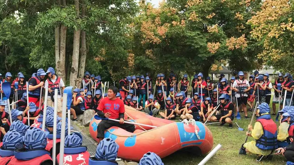 許多遊客穿戴頭盔和救生衣，在綠草如茵的場地與泛舟艇旁集合，期待花蓮瑞穗的親子泛舟活動。