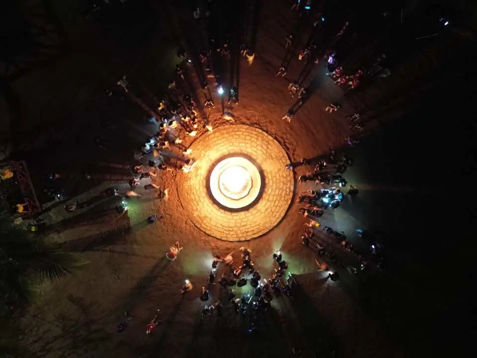 An aerial view of a circular illuminated installation at Nha Trang's 100 Eggs Mud Bath Spa Theme Park at night, surrounded by visitors, creating a festive atmosphere.