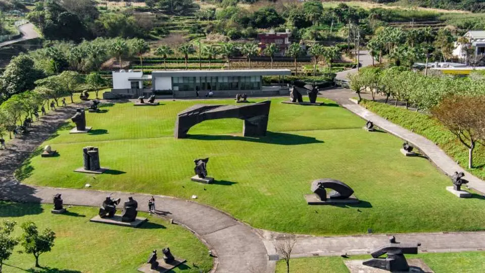 朱銘美術館戶外雕塑公園空拍圖，各式藝術品與廣闊草坪、蜿蜒步道、周圍樹木和諧交融，是絕佳的親子藝術饗宴場所。