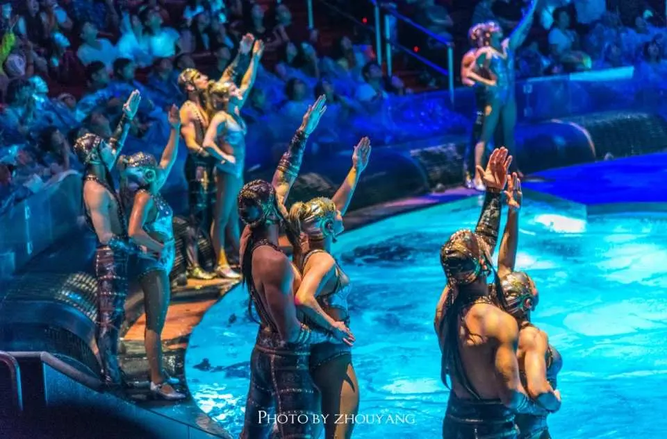 《水舞間》多位身穿華麗服飾的表演者在水舞台邊緣起舞，燈光營造神秘氛圍，展現水上匯演精髓。