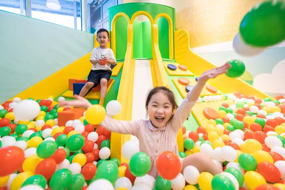 Children happily playing in a vibrant ball pit with a yellow slide in the background at Shanghai LEGOLAND Discovery Center's interactive and joyful play area.