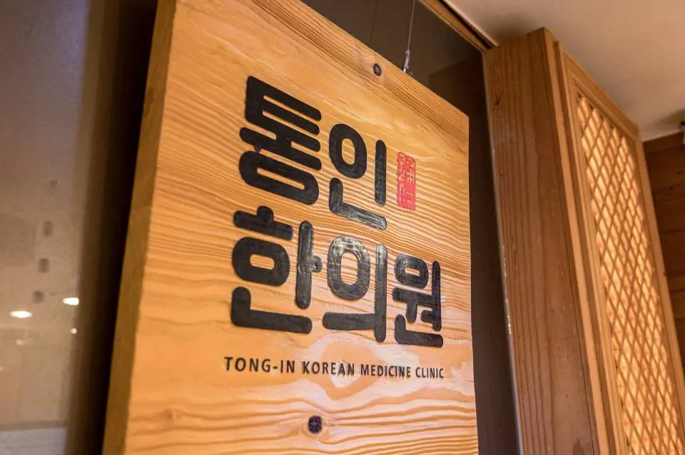 トンイン韓方クリニックの木製看板。韓国語と英語のクリニック名が書かれており、韓国伝統医学と現代の融合したプロフェッショナルなイメージを表現しています。