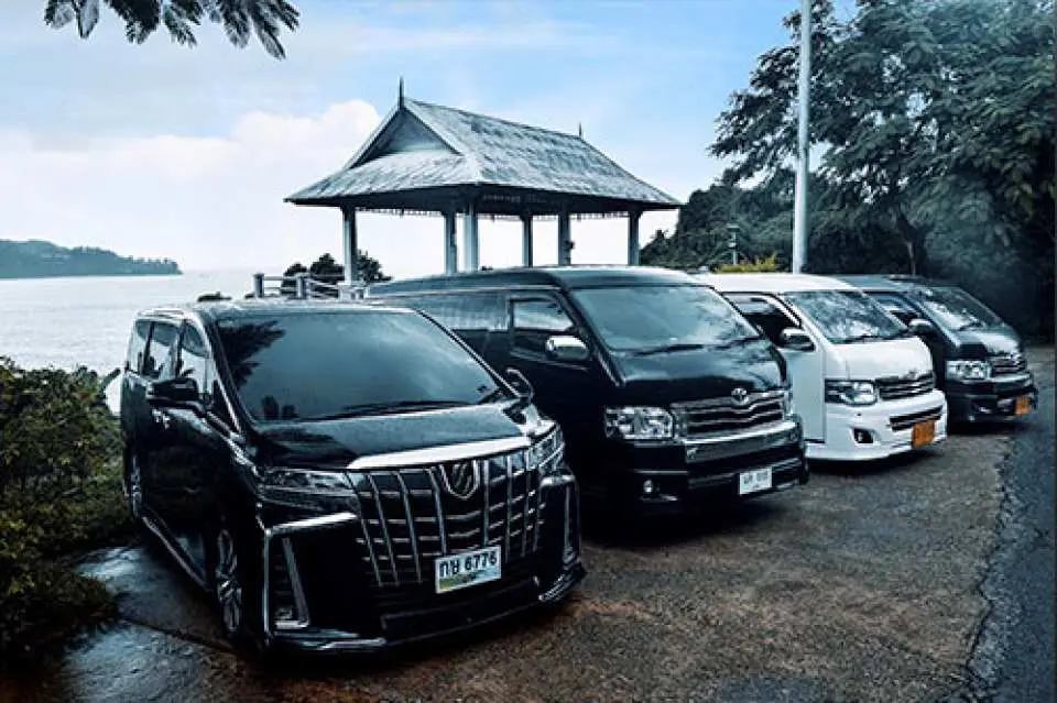 プーケットの海辺にあるタイ風ガゼボの横に駐車された複数の高級プライベートバン。空港送迎や島内観光に信頼性の高い車両を提供します。