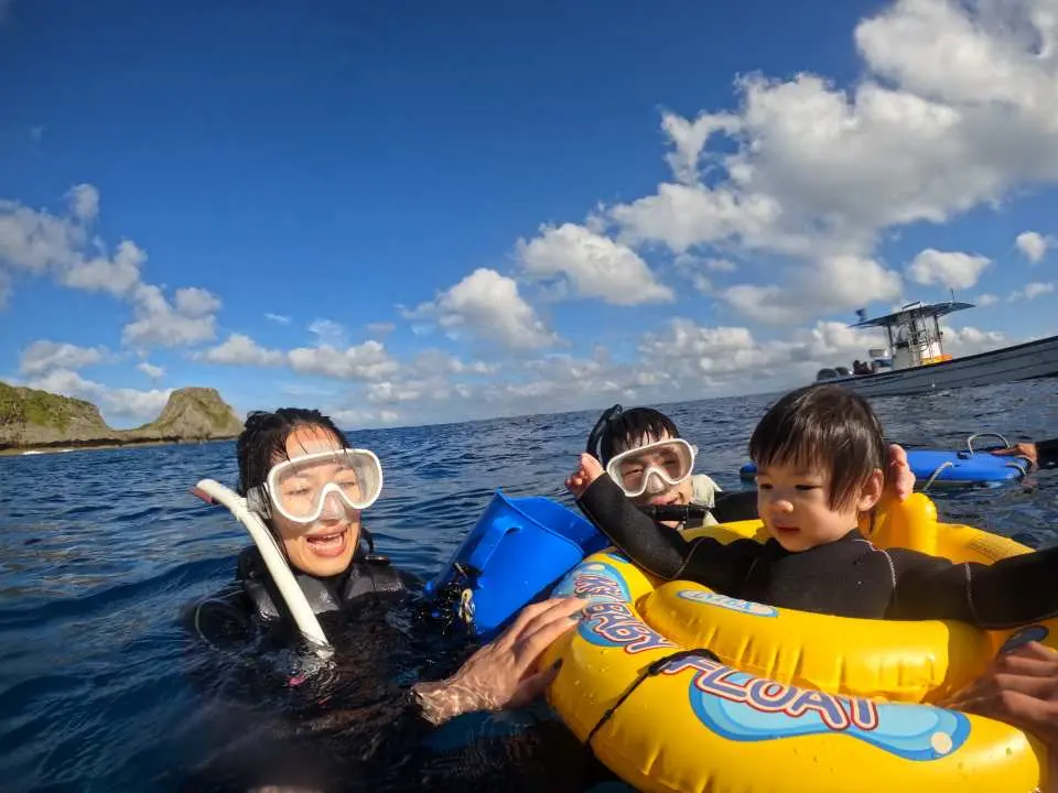 沖縄青の洞窟親子シュノーケリングで、青空と白い雲の下、家族が広大な海で楽しく遊び、ボートダイビングがもたらすリラックスした家族の時間を満喫しています。