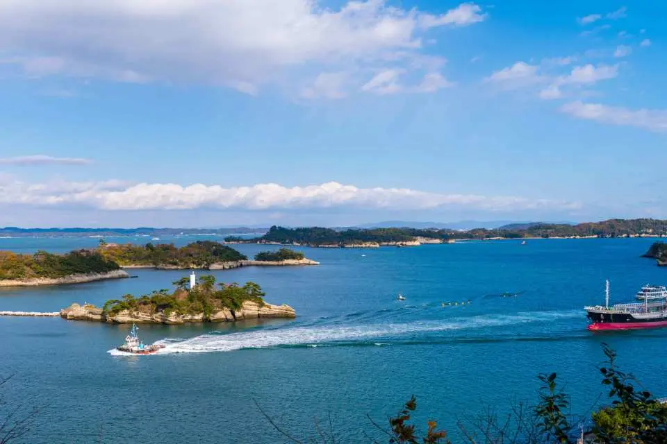 日本三大景松島灣風光，遊船緩駛於湛藍海面，周圍星羅棋布的翠綠島嶼與白色燈塔構成絕美畫卷。