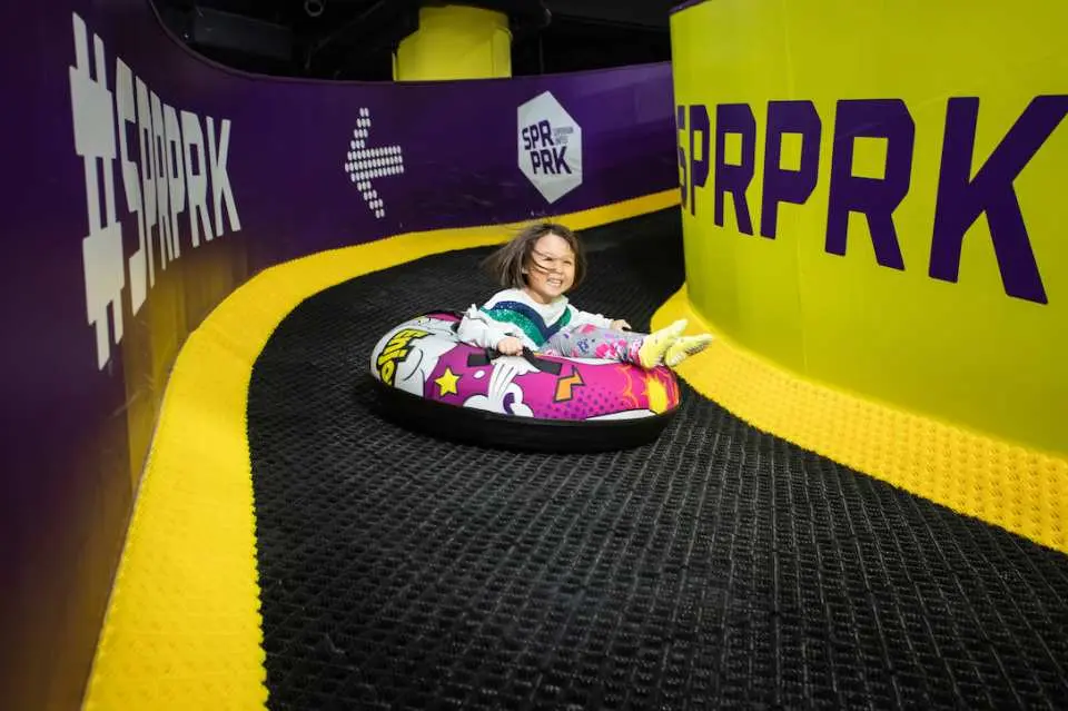 A cheerful child in SuperPark Kuala Lumpur Malaysia enjoying a thrilling ride down an indoor tubing slide in a colorful inflatable float, showcasing family-friendly fun.