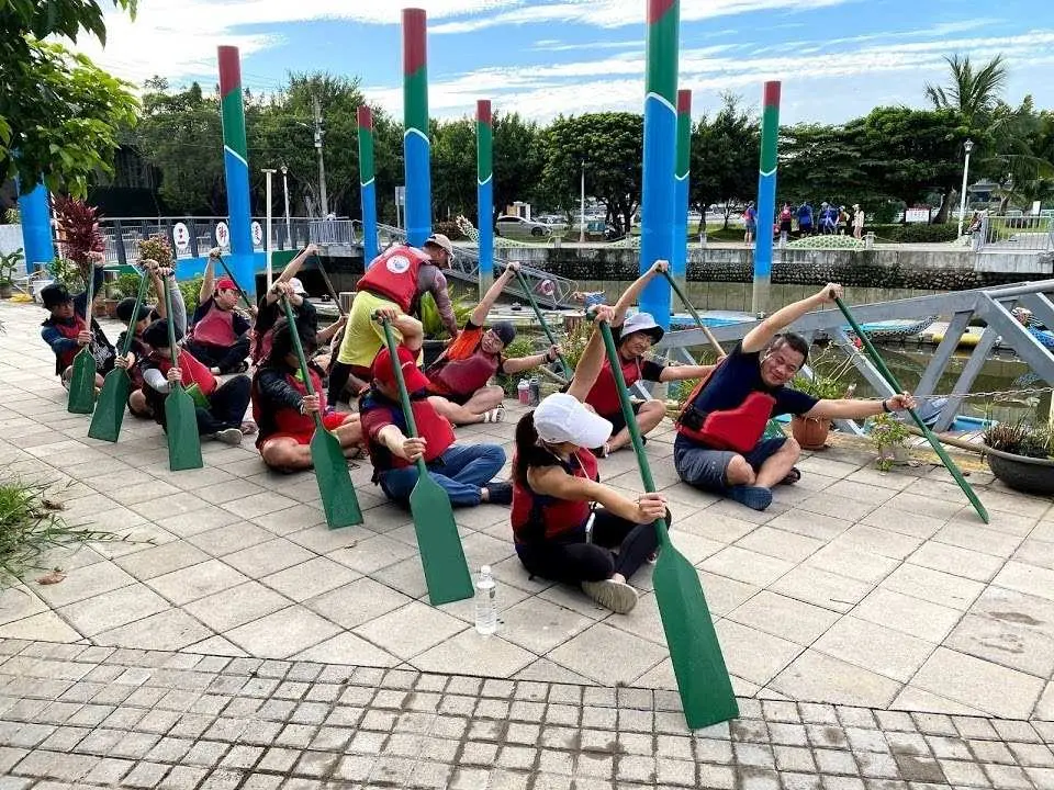 In a Taipei dragon boat experience class, a professional coach guides participants through paddle posture warm-ups and instruction on the shore, ensuring beginners can safely enjoy the water activity.