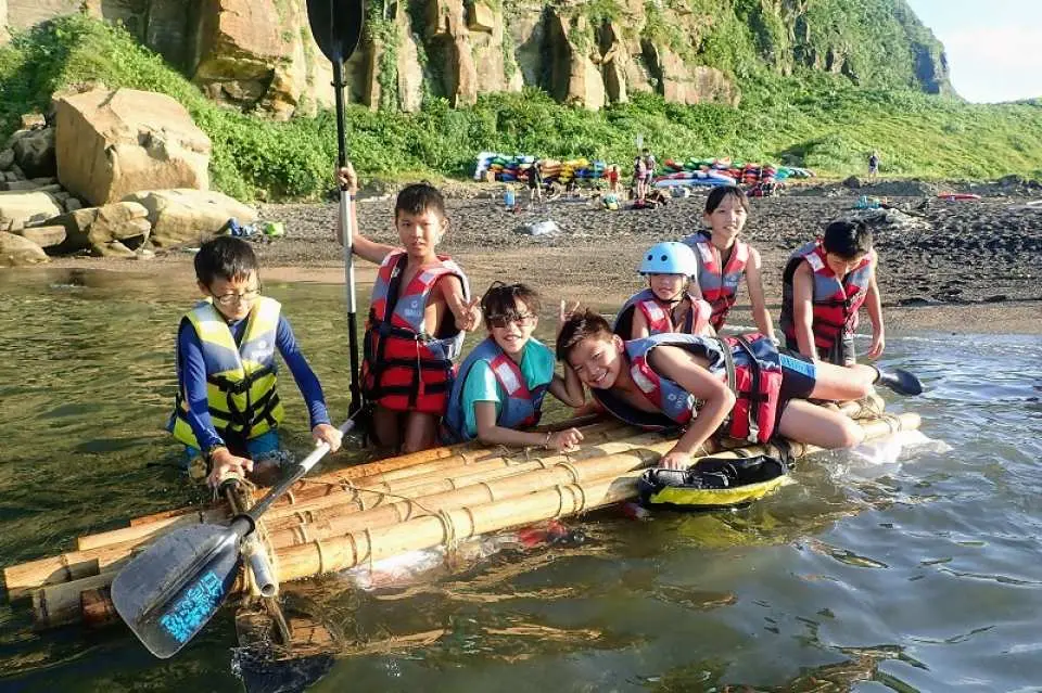 新北貢寮澳底沙灘上，一群學員們身穿救生衣，圍繞著竹筏在淺水區玩耍，享受環保造舟後的團隊水上活動。