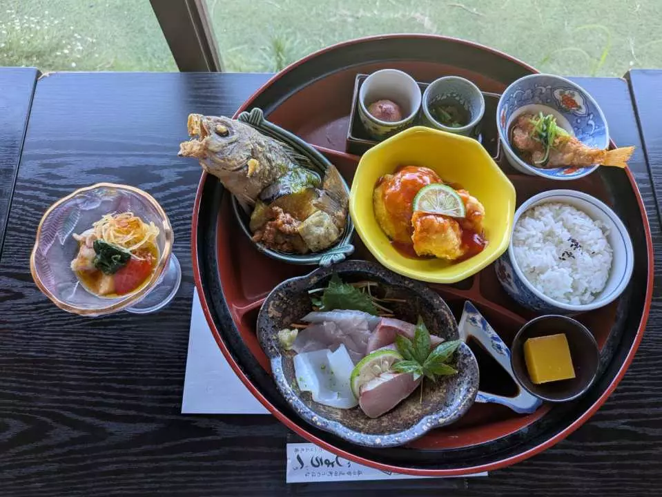 在日本古民家改造的餐厅享用传统日式套餐，丰盛的菜肴摆满漆盘，包含烤鱼、刺身和多样精致小钵，令人食指大动。