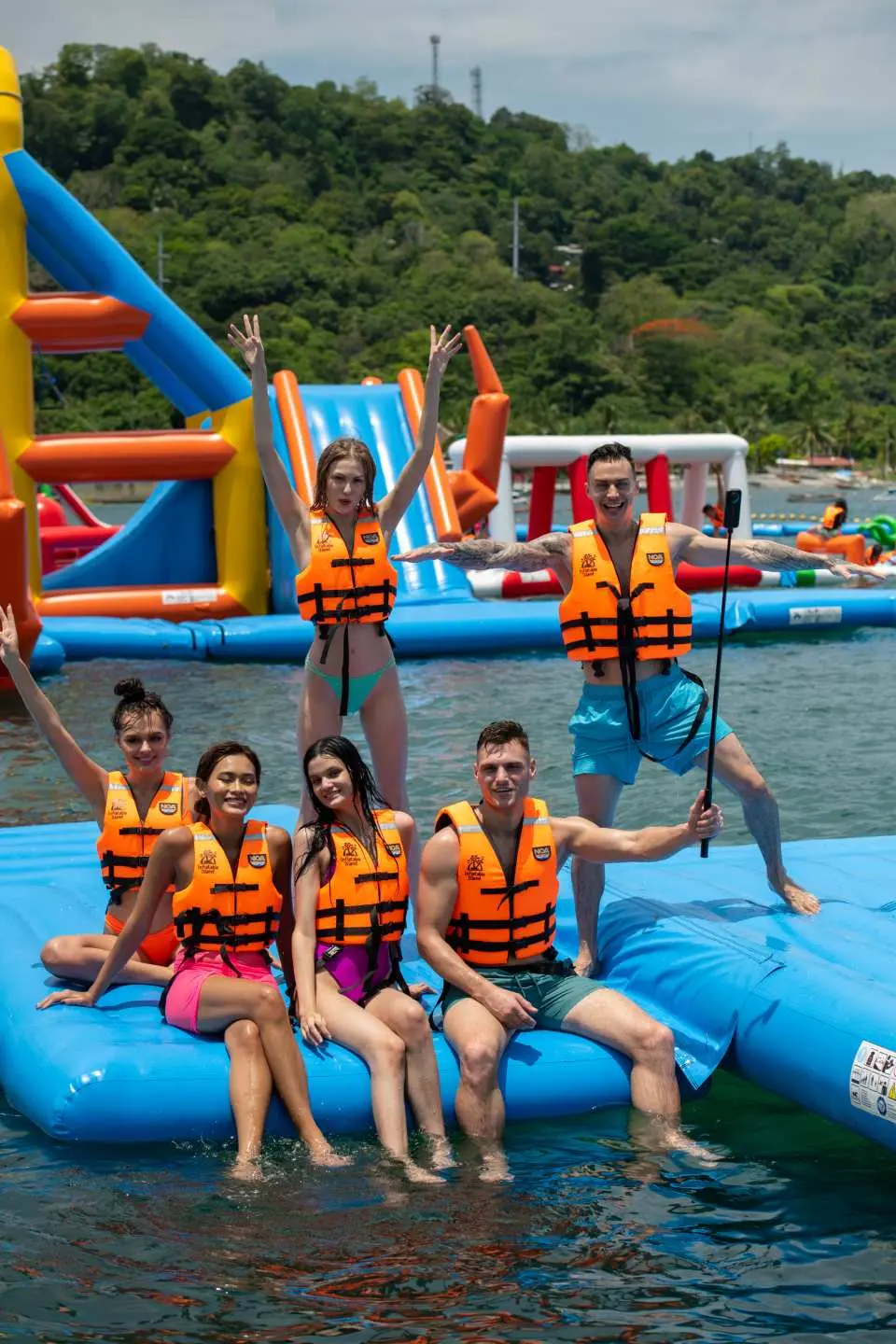 A group of friends in life vests happily pose on a blue inflatable platform at Subic Bay Inflatable Water Park, ready to challenge various water facilities in the park.
