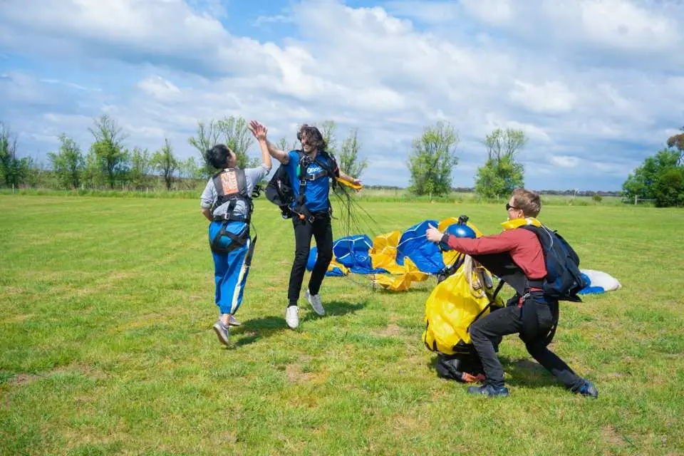 Skydivers and instructors celebrating a successful landing in a sunny green field after a thrilling Great Ocean Road skydiving experience in Victoria, Australia.