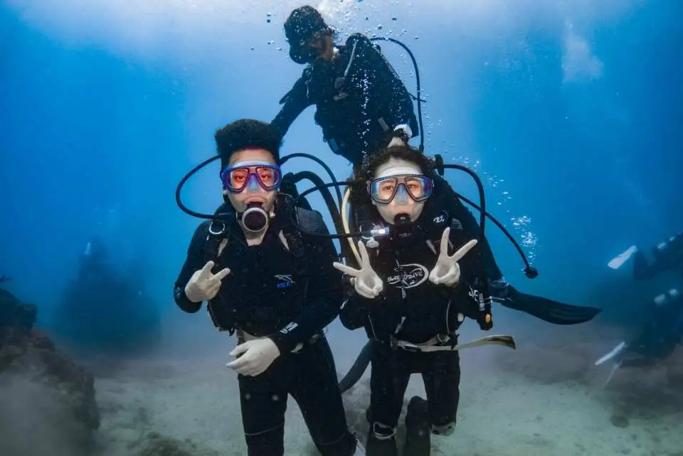 台灣墾丁體驗潛水，兩位潛水學員在專業教練陪同下，開心地在清澈海水中擺姿勢，享受美好水下時光。