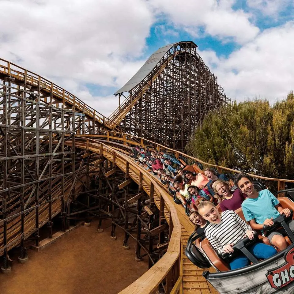 ノッツベリーファームの「ゴーストライダー」木製ジェットコースターで、ゲストは興奮して叫び、急降下のスリルを味わいながら、クラシックな西部テーマエリアの魅力を体験しています。