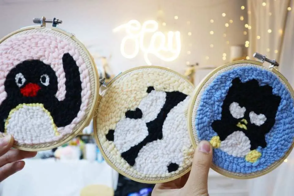 Students at Myosotis.flower's Kwun Tong Russian punch needle embroidery workshop proudly display multiple creative yarn art pieces with various cute designs like penguins and polka dots, showcasing the joy of crafting.