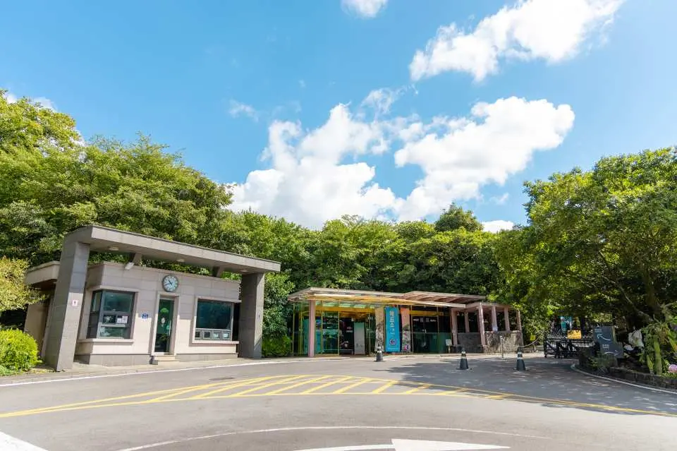 The modern entrance and ticket booth of Jeju World Automobile & Piano Museum, nestled amidst lush green trees under a bright blue sky, welcoming visitors.