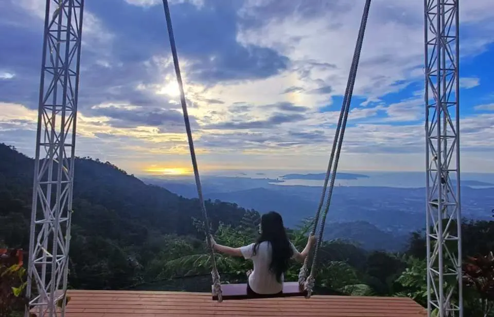 馬來西亞沙巴可可山，遊客坐在巨型鞦韆上，靜靜欣賞日落餘暉灑在海面與山脈的壯麗景色。