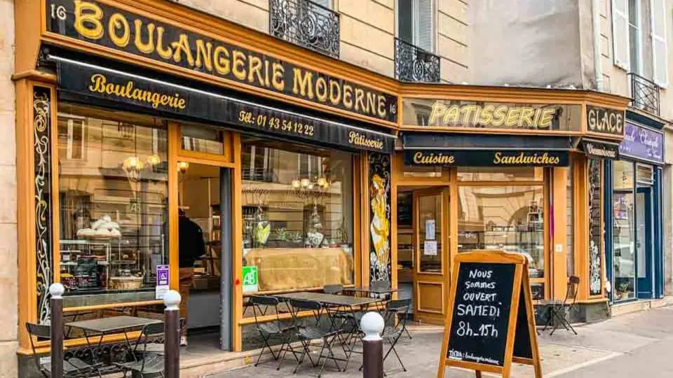 The charming exterior of Paris's 'Boulangerie Moderne' bakery with outdoor seating and tempting pastry displays, an iconic cafe location where Emily and Mindy chatted on the 'Emily in Paris' walking tour.