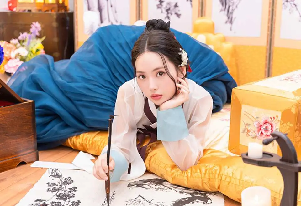A woman in a traditional Hanbok gracefully engaging in calligraphy indoors, showcasing the immersive cultural experience of a Seoul Hanbok photoshoot.