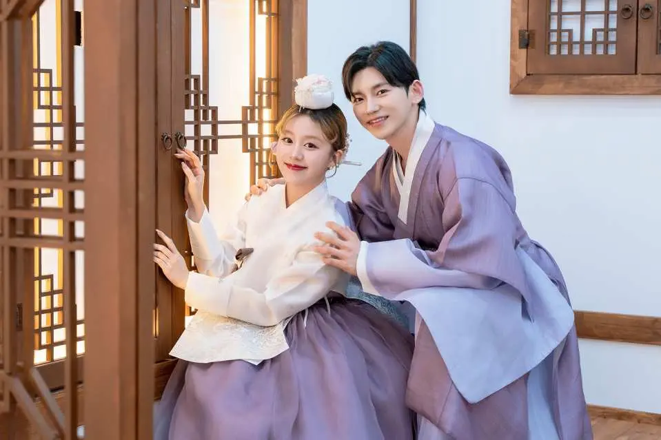 A happy couple in coordinated purple Hanboks posing inside a beautifully decorated Hanok-style studio in Seoul, capturing their memorable Hanbok photoshoot experience.