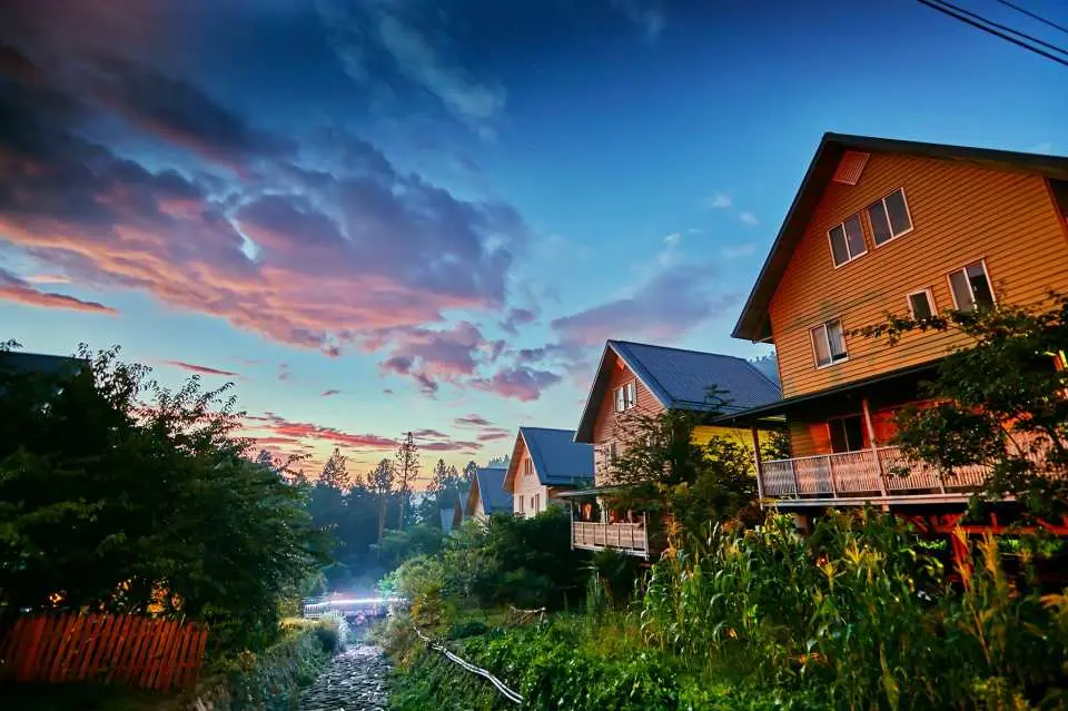 多林车站附近山间的木屋民宿，沐浴在夕阳余晖中，粉橘色的云彩装点天空，提供嘉义包车一日游的宁静住宿氛围。