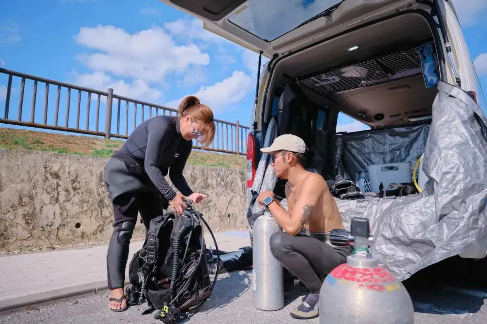 沖縄PADIダイビングコース。生徒とインストラクターがダイビングポイントの傍らでフル装備を準備し、美しい海への水中探検に備える。