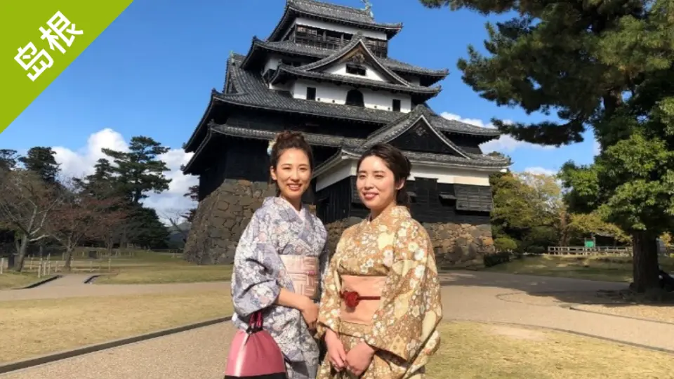 在岛根松江城城下，两位身着和服的女子对着镜头微笑，享受日本历史文化之旅的愉快时光。