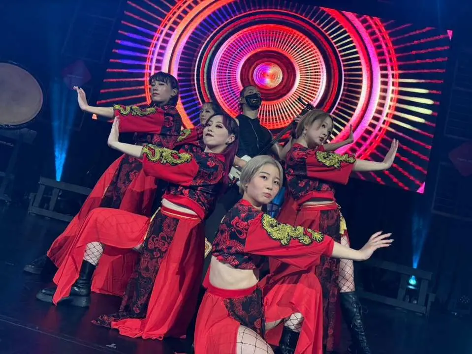 大阪之夜融合表演中，身穿现代红黑服饰的女性舞者在动感舞台上展现活力舞蹈，背景是迷幻圆形图案。