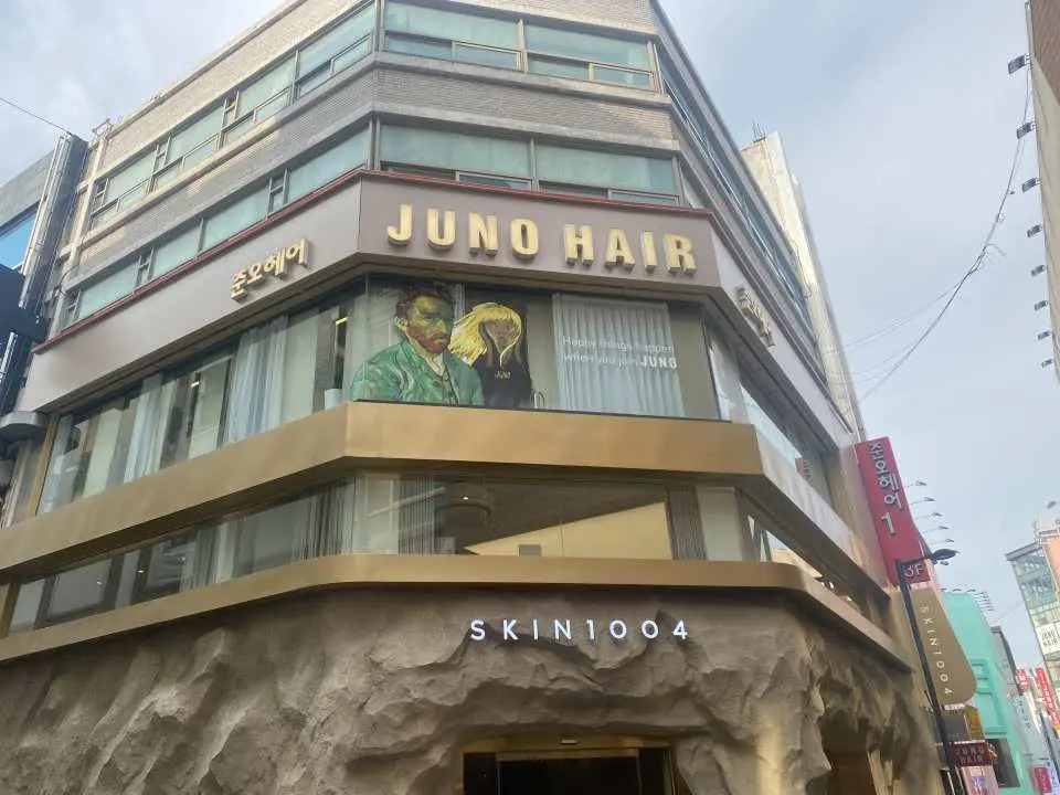 Exterior view of JUNO HAIR Myeongdong in Seoul, South Korea, with its prominent metallic sign, showcasing its landmark status as a renowned hair salon.