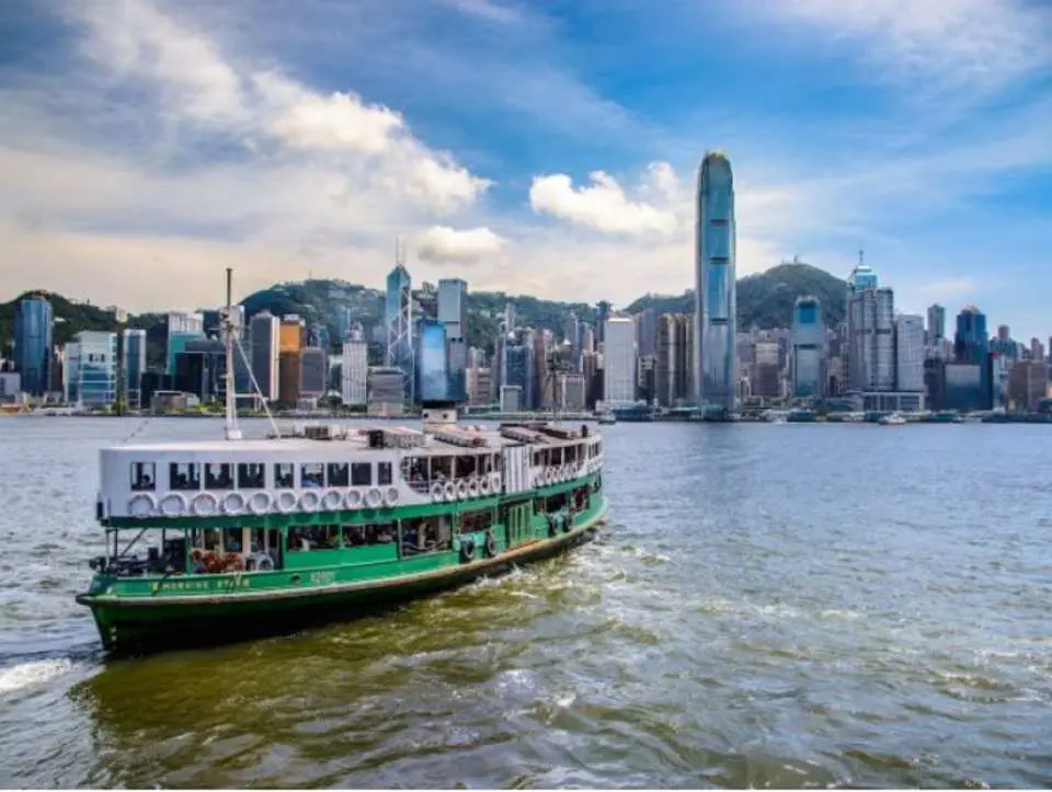 經典綠白相間嘅天星小輪行駛於維多利亞港上，背景為香港島壯麗嘅天際線，提供絕佳海港巡遊體驗。
