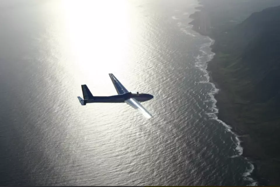A dark blue glider soaring silently over Hawaii's glittering ocean, with the sun's reflection creating a dazzling streak, offering an unforgettable unpowered flight experience.
