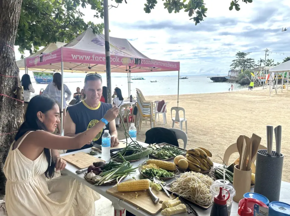 Participants at a Siargao Island beach cooking class prepare traditional Filipino dishes hands-on, guided by a local chef, utilizing an array of fresh vegetables, fruits, and other ingredients.
