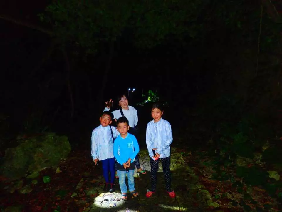 An adult and three children posing with flashlights in the dark during a Miyakojima night jungle adventure, enjoying the fun of spotting nocturnal animals.
