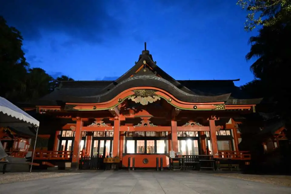 青岛神社主殿夜晚光彩夺目，传统屋檐与橘红色彩，AI语音导览带来丰富故事。