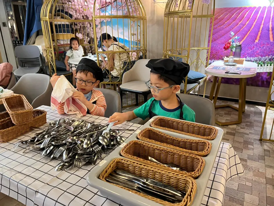 Two dedicated boys in Mr.O chef hats and aprons learning restaurant etiquette by organizing cutlery during the "小店長體驗日" in Lai Chi Kok.