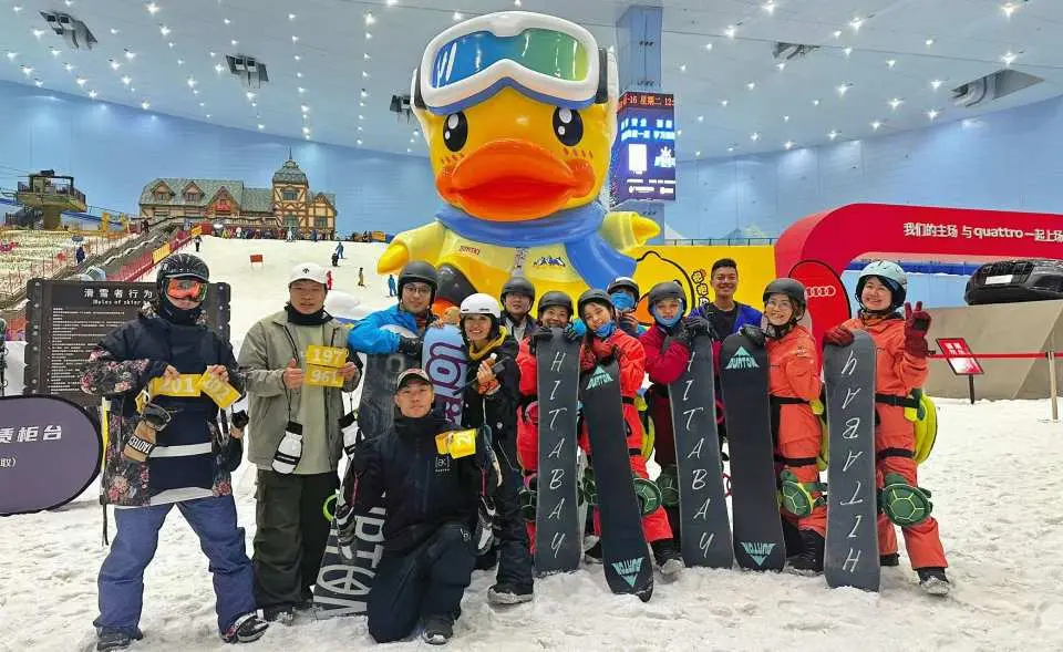 一大群滑雪愛好者在深圳華發冰雪熱雪奇蹟滑雪場內，與巨型鴨子吉祥物合照，展示團體滑雪歡樂氣氛及滑雪場特色。